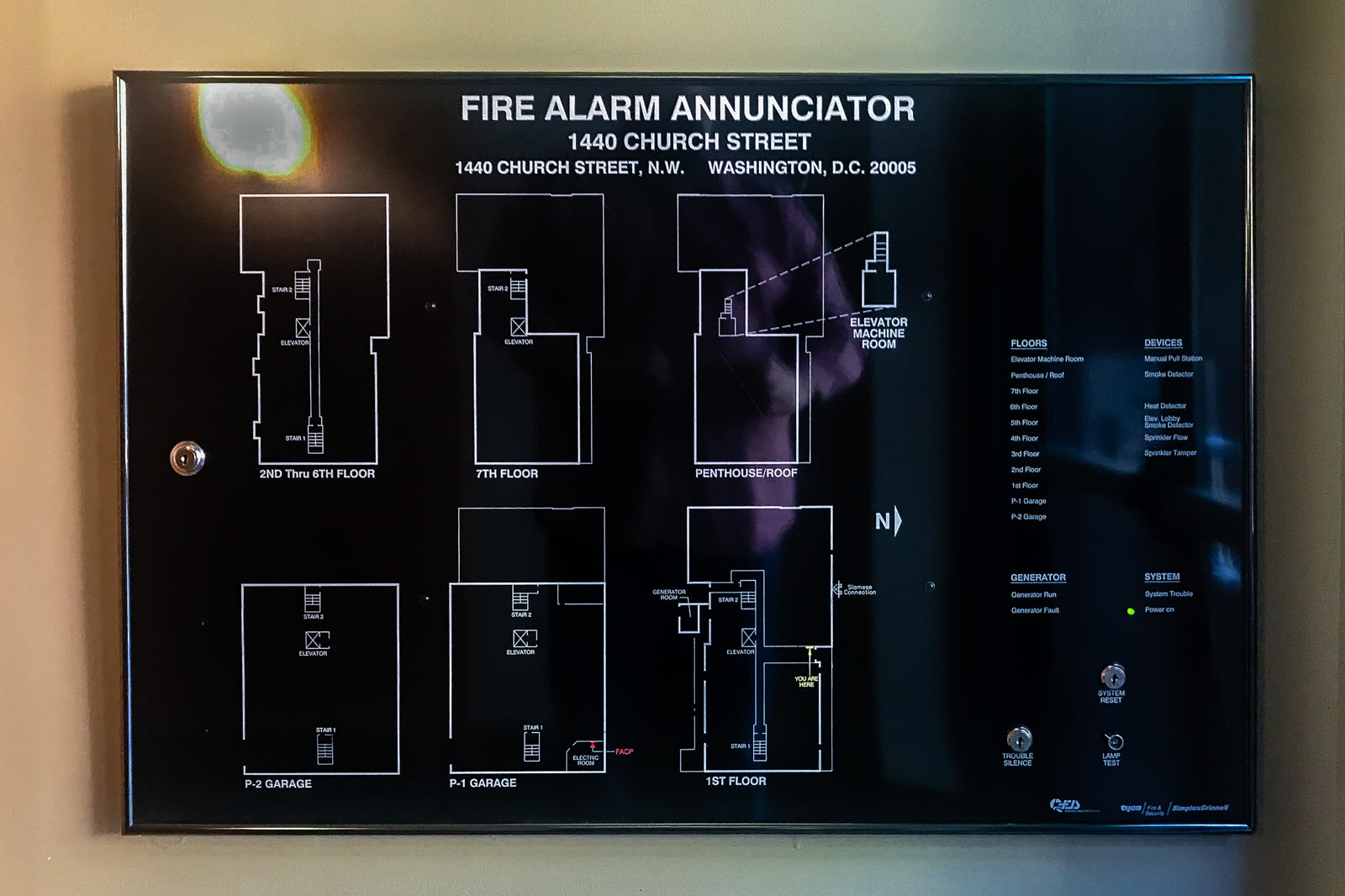 A wall-mounted fire alarm annunciator panel showing a building's floor plans and a legend of the zones it monitors.
