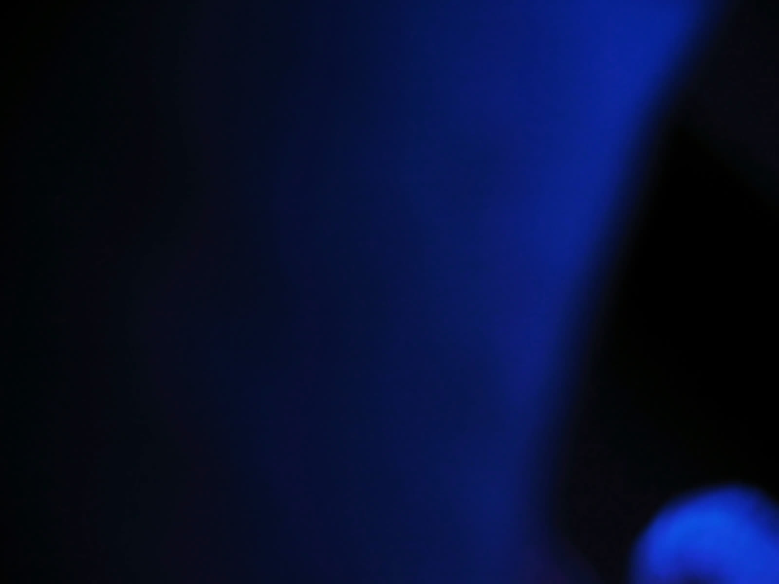 A dark blue abstract field, almost entirely empty, with a single soft smear of lighter blue.