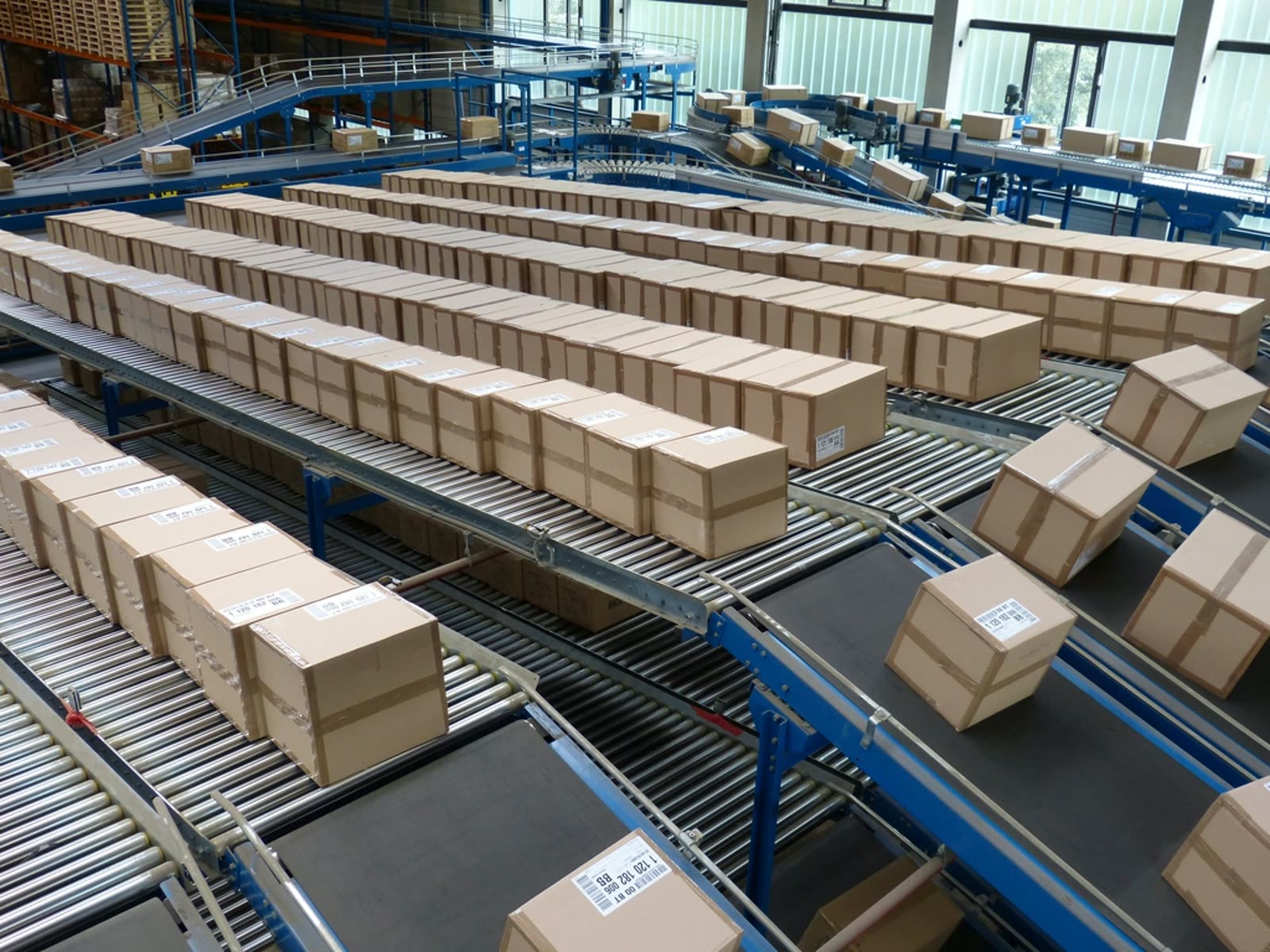 Cardboard boxes moving along rows of roller conveyors in a warehouse.