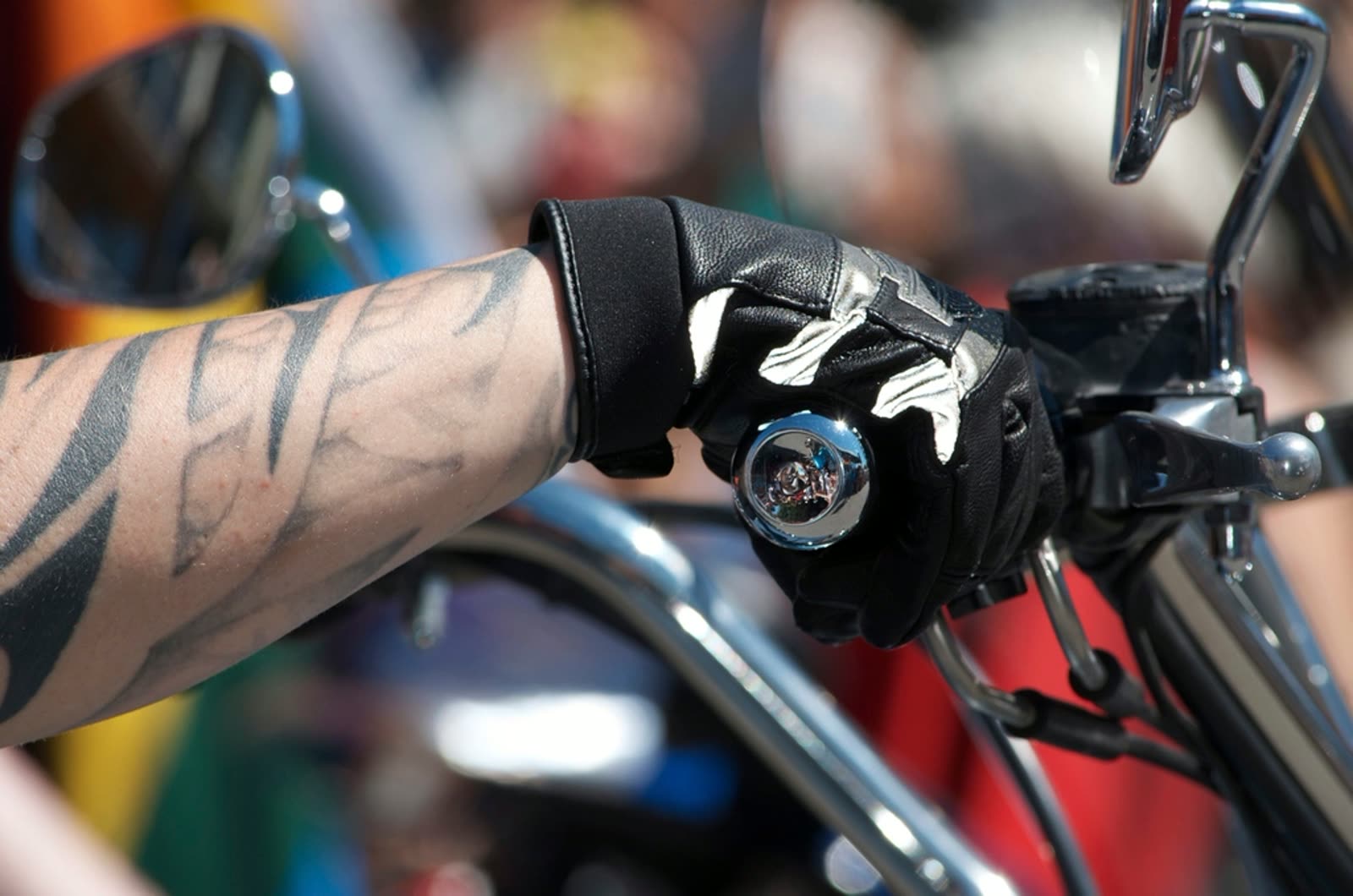 A gloved hand resting on the handlebar of a chromed cruiser motorcycle.